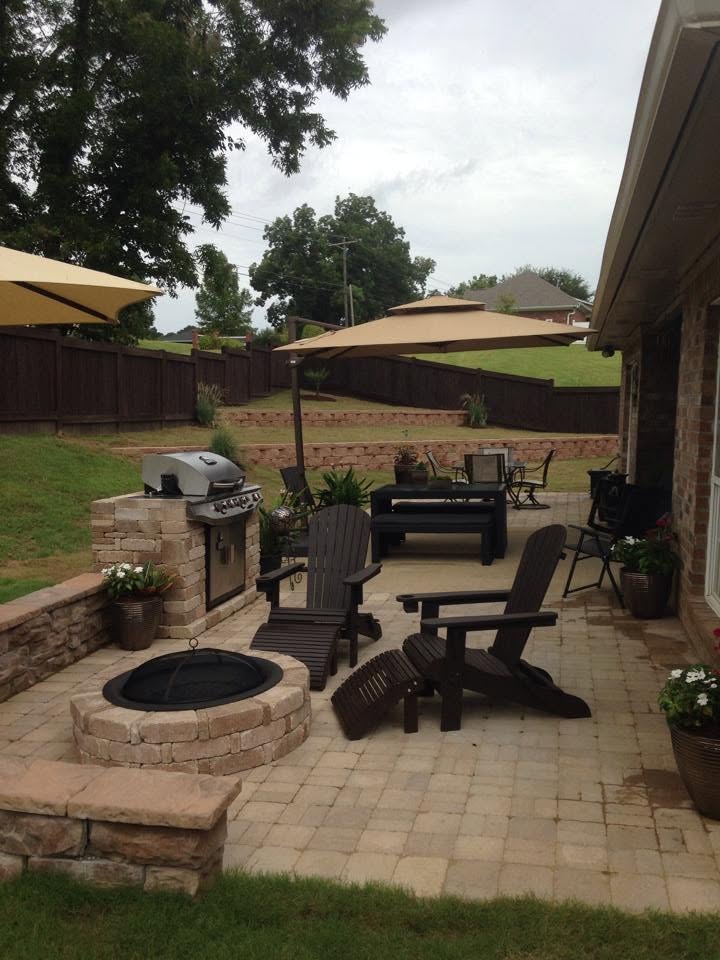 Patio living space with stone fire pit, outdoor grill, dining area, and terraced backyard retaining walls