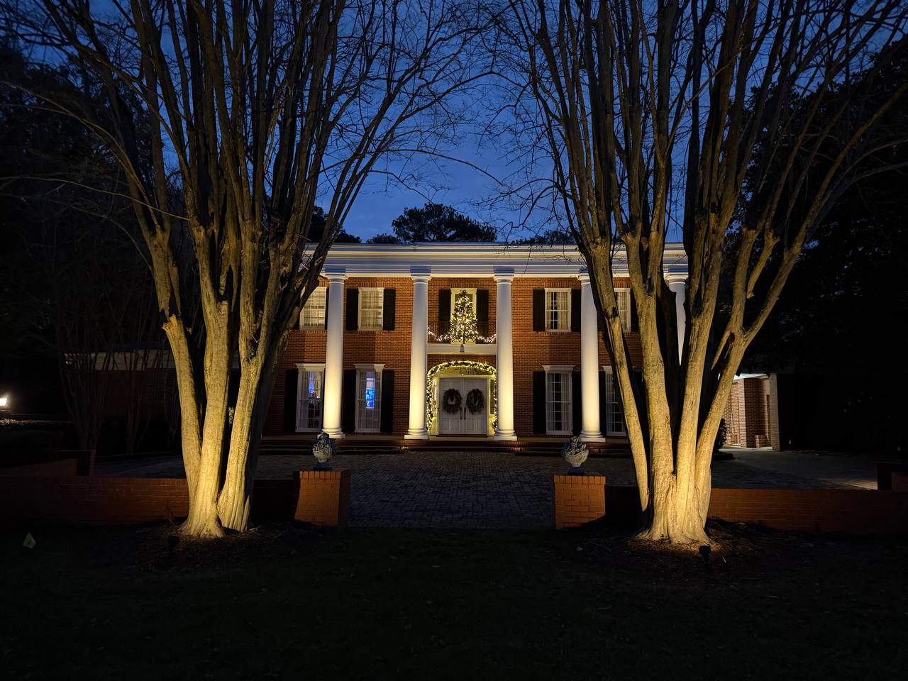 Brick colonial estate framed by illuminated trees and warm architectural lighting at dusk