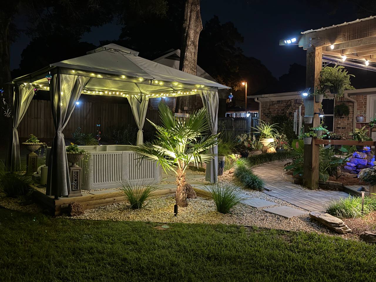 Spa canopy and nearby palm illuminated at night with gravel, paving, and planted borders